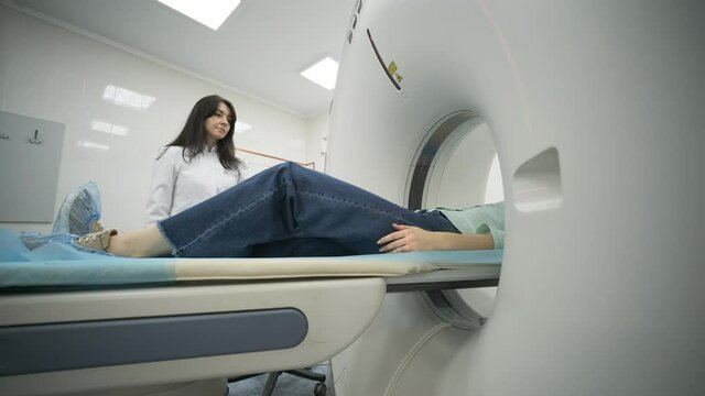 Female patient is undergoing CT or MRI scan under supervision of a radiologist in modern medical clinic. Patient lying on a CT or MRI scan bed, moving inside the machine.