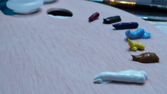 the girl's hand squeezes yellow oil paint onto a wooden paint palette.