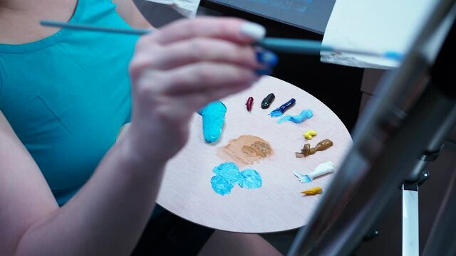 the girl takes the paint with a brush from the palette. draws on canvas on a tripod. the view from the top.