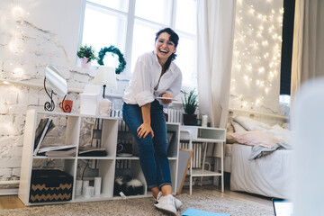 Smiling woman standing near shelves with smartphone