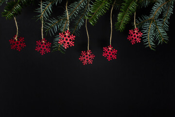 Christmas winter greeting card with evergreen branches and hanging red wooden snowflakes on black background. Photo with copy blank space.