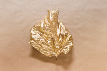 Creative composition with single one leaf dyed with golden metallic color on kraft paper background.