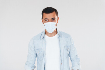 In protective mask. Young handsome man standing indoors against white background