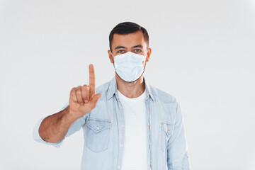 In protective mask. Young handsome man standing indoors against white background