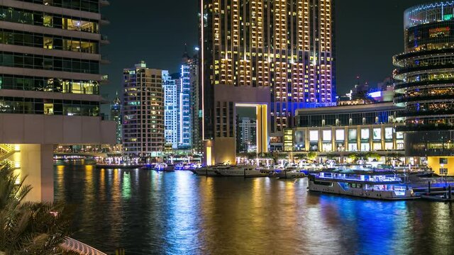 Dubai Marina waterfront with yachts and modern towers from bridge in Dubai night timelapse, United Arab Emirates. Palms and caffes