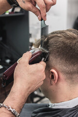 a barber in a barbershop cuts a man's hair. hands holding an electric hair clipper. professional haircut at home during quarantine and pandemic