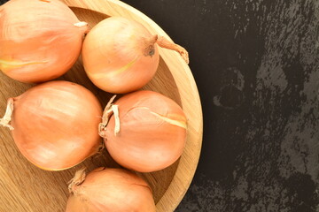 Several ripe organic onions on a round wooden tray, close-up, on a slate board.