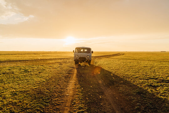 Adventure Spirit. Old Post Soviet Off-road Vehicle Car UAZ Bus Rides On A Country Road.  Warm Beautiful Sunset Sepia Light And  Raining. Backlight. Romantic Nostalgic Movie Cinematic Horizontal Photo