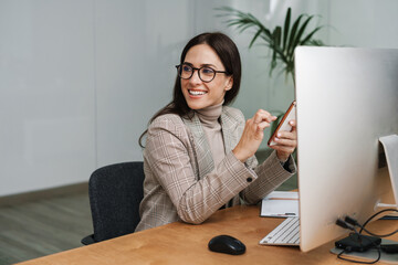 Smiling woman using cellphone while working with computer and planner