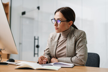 Serious charming woman writing down notes in planner while working