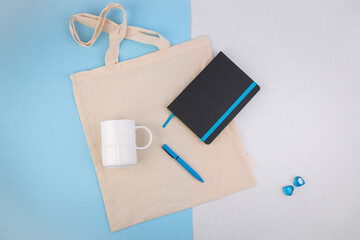 White rag bag with black notebook, blue handle and white cup
