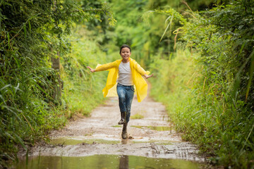 happy little asian  girl running and jumping in puddles after rain in summer. child play in autumn rain. kid playing on the nature outdoors. girl is wearing yellow raincoat and enjoying rainfall..