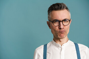 Displeased grey-haired man in eyeglasses grimacing and looking at camera
