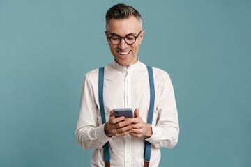 Happy grey-haired man in eyeglasses smiling and using cellphone