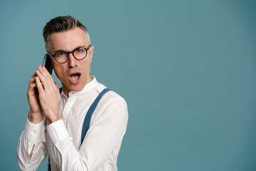 Shocked grey-haired man in eyeglasses talking on cellphone