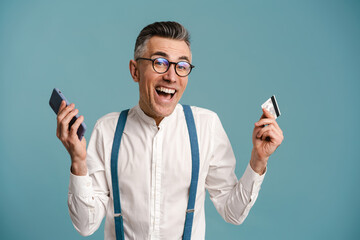 Excited grey-haired man posing with cellphone and credit card