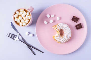 Top view still life of a bitten cake on a pink plate, cutlery and a cup of cocoa with marshmallows....