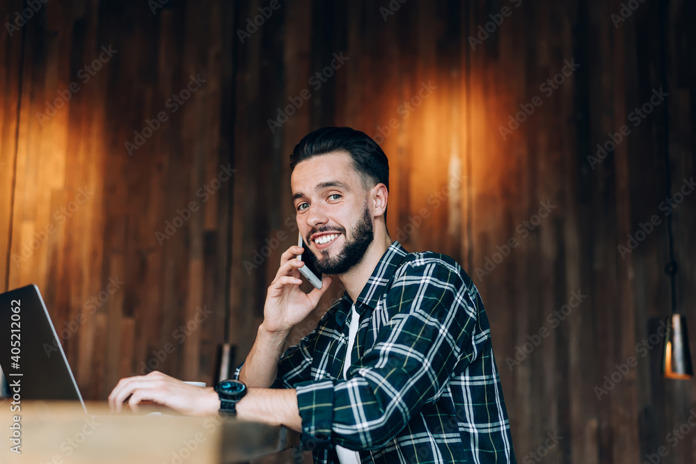Poster portrait of cheerful man making positive cell conversation during distance job in coworking space, j
