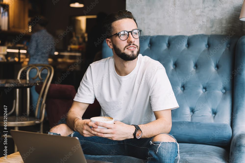 Poster thoughtful male programmer with cappuccino cup in hands thinking about project idea during remote jo