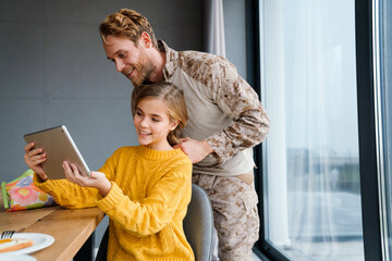 Military man doing hair of his daughter while she using tablet computer