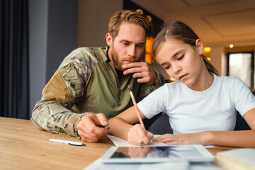 Masculine focused military man doing homework with her daughter at home