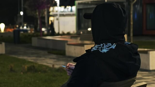 A man in black hood smoking on the street at night in Bucharest, Romania