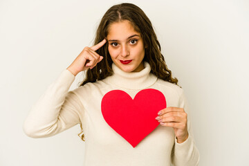 Fototapeta na wymiar Young caucasian woman holding a heart valentines day shape isolated pointing temple with finger, thinking, focused on a task.