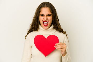 Young caucasian woman holding a heart valentines day shape isolated screaming very angry and aggressive.