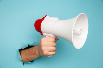 Man's hand arm hold megaphone isolated through torn blue background.