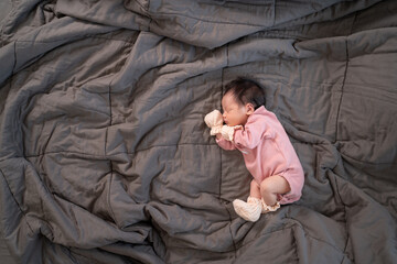 Obraz premium asian baby infant wearing gloves and socks sleeping on gray bed. studio shot.
