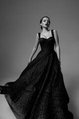 Full length studio fashion portrait. Elegant woman in black shiny evening dress. Dynamic shot....