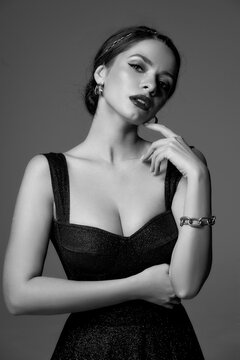 Breast up portrait of young elegant sexy woman in black shiny evening dress with decolette against grey background, Beautiful caucasian girl with perfect makeup and hair in bun.
