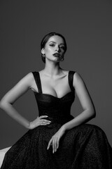 Elegant woman with perfect make-up and brunette hair in a bun in black shiny evening ball gown...