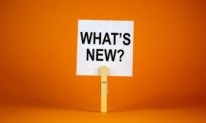 What is new symbol. White sheet of paper on wooden clothespin. Words 'what is new'. Beautiful orange background. Business and what is new concept, copy space.