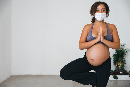 Portrait of a young pregnant woman engaged in yoga exercise during pregnancy wearing face mask to protect herself from Covid-19 infection, Coronavirus