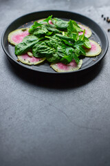 Watermelon radish fresh salad chinese daikon Slices pink fruit, green leaves spinach lettuce on the table healthy meal snack top view copy space food background keto or paleo diet