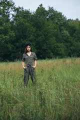Woman on nature holds his hands in the pockets of green overalls in the meadow 
