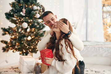 Man makes surprise for his girlfriend. Young romantic couple celebrates New year together indoors