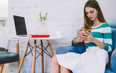 Thoughtful young female using smartphone while working at cafe