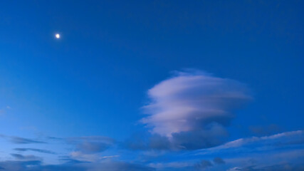 Lenticular cloud formation with the moon in a deep blue sky
