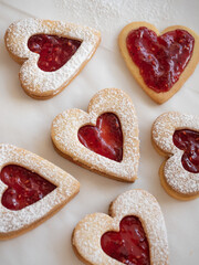 Homemade heart shaped cookies with raspberry jam sprinkled with icing sugar on white background in morning light