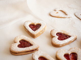 Homemade heart shaped cookies with raspberry jam sprinkled with icing sugar on white background in morning light
