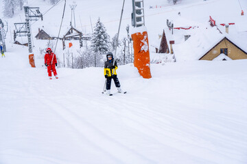AURON, FRANCE-01.01.2021: Professional ski instructor and child lifting on the ski drag lift rope to the mountain during snowfall. Family and children active vacation concept. Blurred focus background
