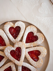 Homemade heart shaped cookies with raspberry jam sprinkled with icing sugar on white background in morning light