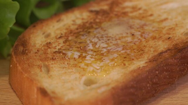 Time lapse of butter melts on hot toast on background of green lettuce. Fresh bread concept for breakfast. Snack food close up