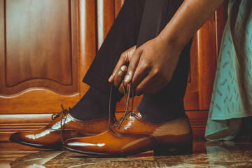 man's arms lightly tying shoelaces next to a clothes closet
