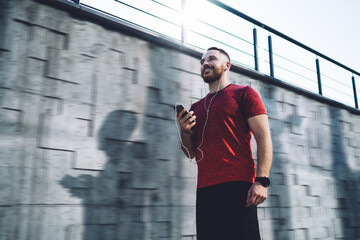 Optimistic sportsman standing with phone and earphones