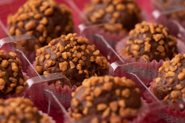 balls of chocolate with peanut praline in a rectangle transparent box on red background, close up view
