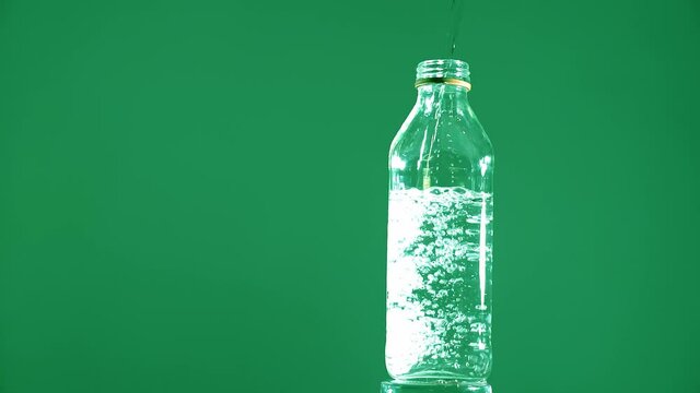 transparent glass bottle being filled with water on color background