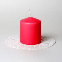 Single thick pink aromatic candle on white openwork paper napkin on gray background side closeup view